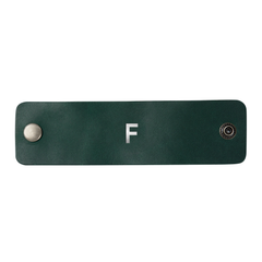 Set of two emerald leather napkin rings with antique snaps, personalized with an initial, on a dinner table