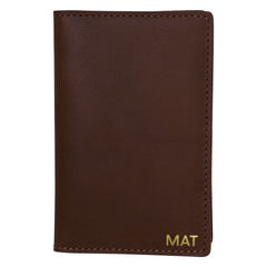 Chocolate full-grain leather passport cover personalized with gold foil initials, next to a pen on marble